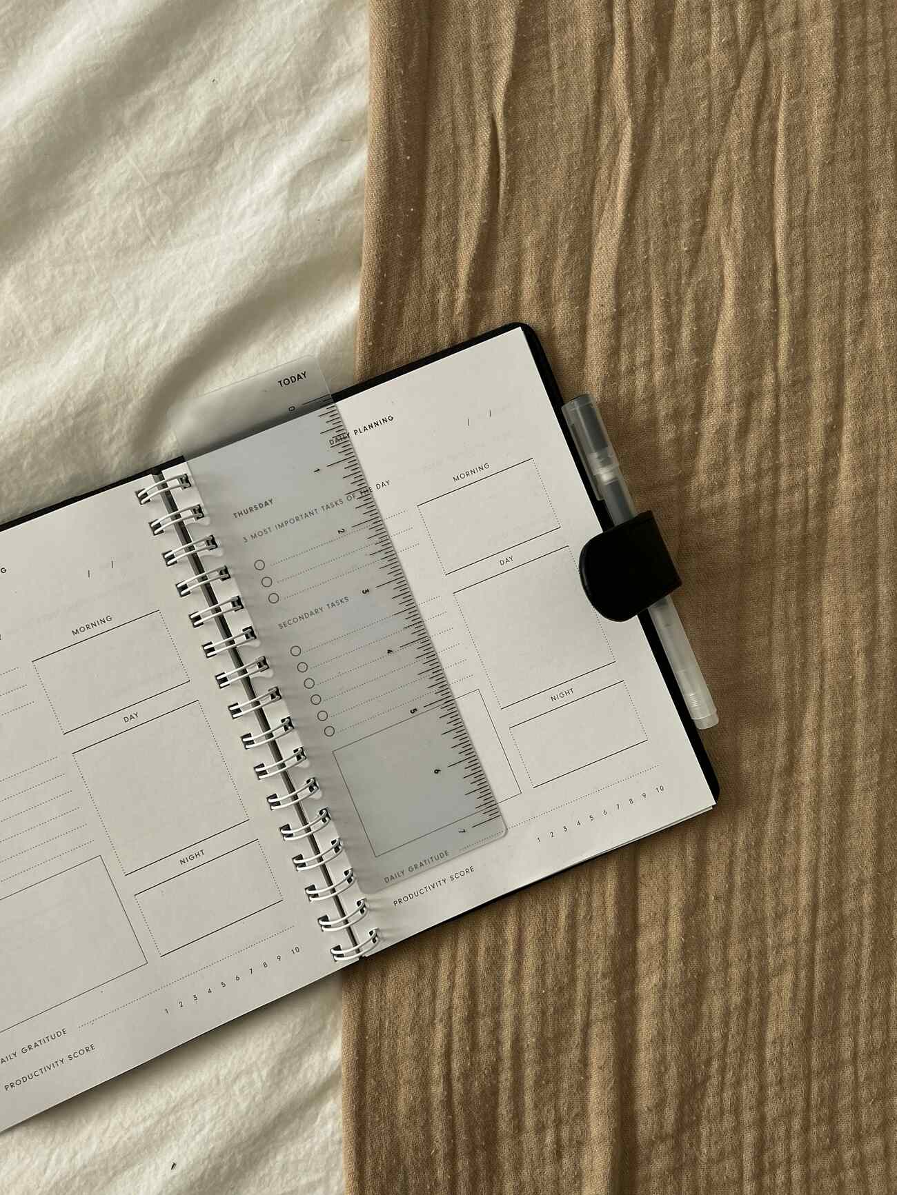 A planner, pen, scale, and notepad arranged on a made bed.