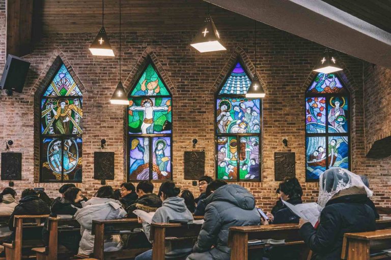 People seated in a church, surrounded by colorful stained glass windows