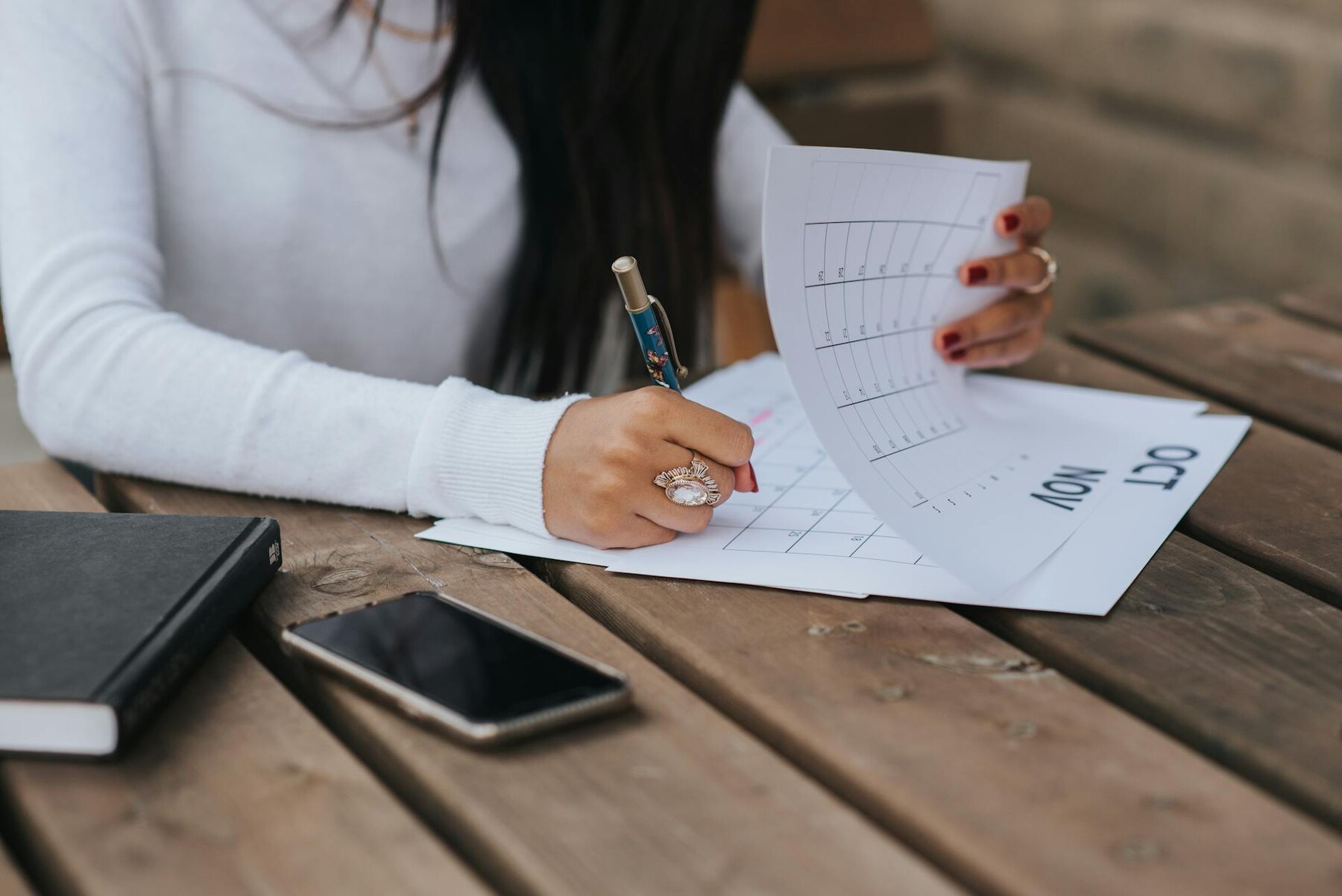 A woman writing on a calendar while holding papers and a pen