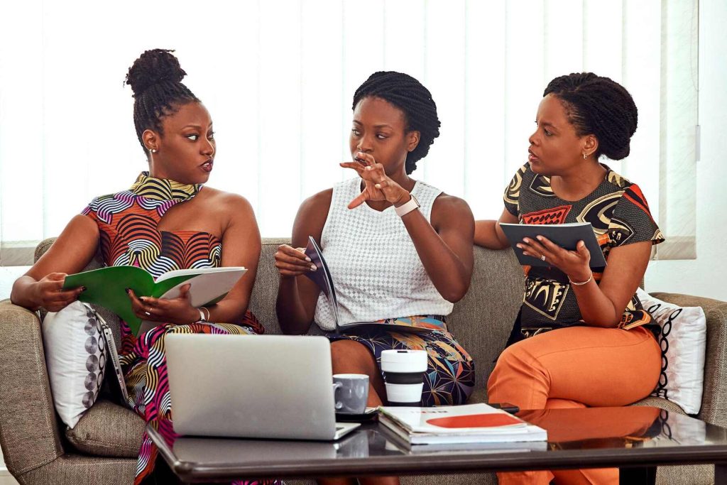 Three women having a discussion on a couch, surrounded by notebooks and a laptop