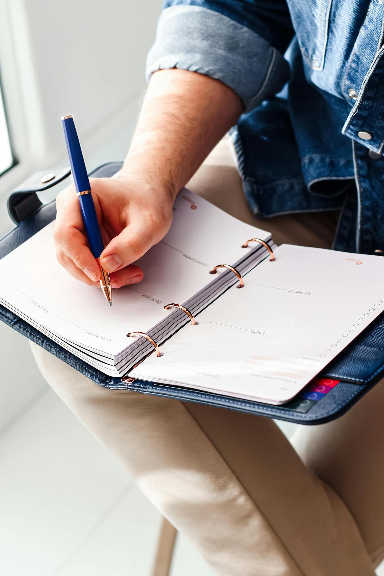 A person writing in a planner with a blue pen