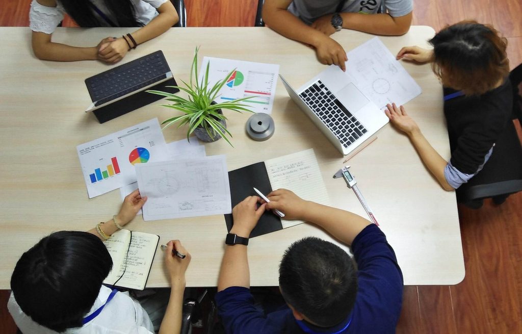 Overhead view of a collaborative work meeting with multiple people discussing data charts and documents